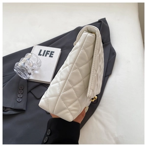 Detail of white quilted crossbody bag showing layered side gussets and golden twist lock