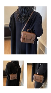 Close-up of brown pebbled leather texture and gold buckles on a small square handbag