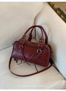 Detail of burgundy Boston bag with silver grommets and woven leather handles on sofa