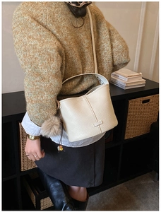 Detail of cream lychee leather bucket bag with plush pompom charm and shoulder strap