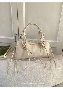 Close-up of beige Boston bag featuring woven leather ties and long fringe tassels