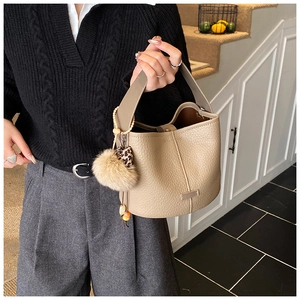 Close-up of khaki bucket bag with lychee texture and soft yellow pom-pom charm