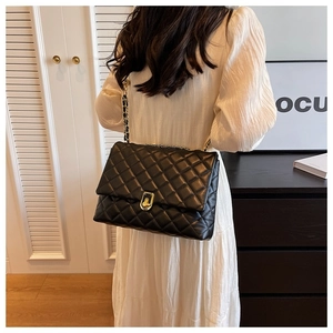 Close-up of black quilted chain bag featuring golden metal turn-lock and leather strap