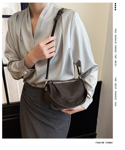 Detail of coffee brown crossbody bag with lychee texture and silver logo plate