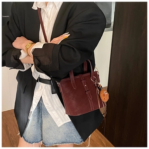 Detail der weinroten Vintage-Eimertasche mit Gürtelschnalle und Plüsch-Keksanhänger