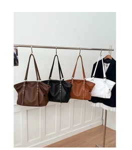 Four large faux leather tote bags in black, brown, and white hanging on a metal rack