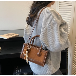 Détail du sac à main vintage marron avec perles décoratives et logo sur un support noir