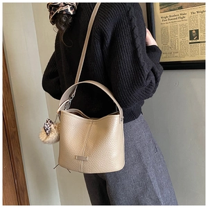 Detailed texture of beige pebbled leather bucket bag with leopard bow and plush charm
