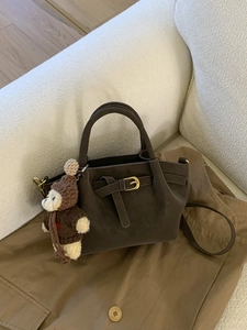 Vintage dark brown matte handbag with metal buckle and cute crochet bear charm on a sofa