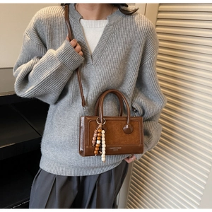 Gros plan d'un sac à main vintage en cuir marron avec perles en bois sur un pull gris