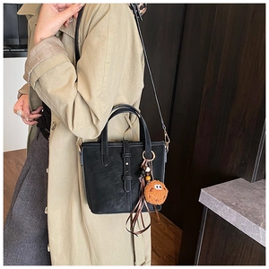 Détail d'un sac seau noir avec un charme orange sur un mannequin en manteau