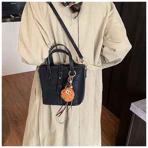 Détail du sac seau noir en daim avec un charmant pendentif en peluche sur la poignée