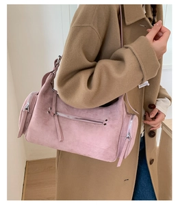 Detail of pink suede cylindrical shoulder bag with metal zippers shown on a model