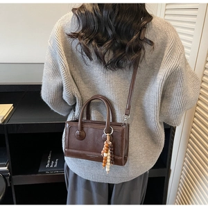 Détail du sac vintage marron avec texte FASHION & BAGS et breloque à pampilles en perles