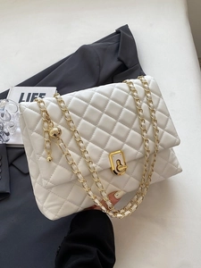 White quilted shoulder bag with gold chain strap and turn-lock closure on grey suit