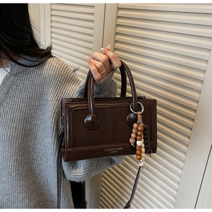 Détail du sac bandoulière vintage marron avec pendentif perlé et lettrage de marque