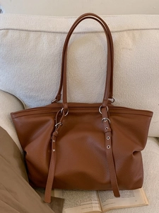 Brown litchi grain faux leather tote bag with silver buckles on white sofa