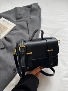 Vintage black crossbody bag with gold buckles on elegant fabric and blazer background