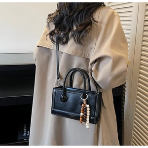 Détail d'un sac à main noir en simili cuir avec gland en perles de bois et logo élégant