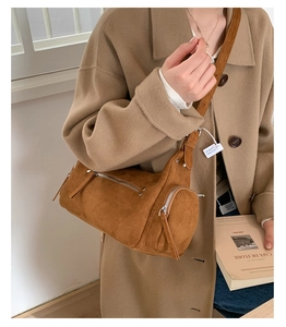 Close-up of a vintage caramel suede cylinder crossbody bag with zipper details and long strap