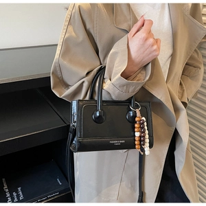 Vue détaillée du sac à main noir mat avec pendentif en perles et doubles poignées rondes