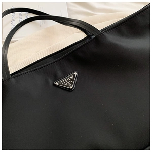 Detail of black oxford tote bag featuring a metallic triangle logo on textured material