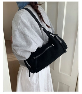 Detail of black suede-style cylinder bag with silver zip pockets and adjustable strap