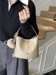 Minimalist beige leather bucket bag with textured finish and leopard heart charm detail