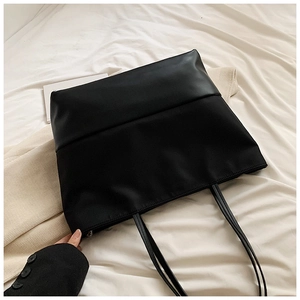Detailed view of black tote bag with matte leather and fabric patchwork on white fabric