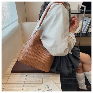 Detail of a brown woven leather tote bag with Intrecciato style and cylindrical handle