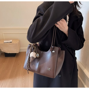 Detail of dark brown leather tote bag with letter branding and plush ice cream charm
