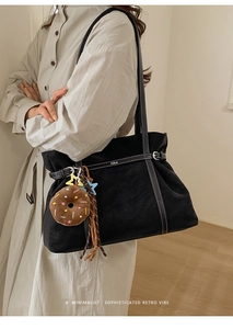 Detail of black suede tote bag with white stitching and decorative donut plush pendant