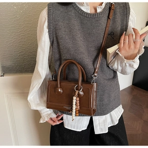 Détail du sac à main en cuir marron foncé avec doubles anses et accessoire perlé bohème