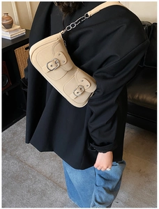Detail of beige shoulder bag with buckle pockets worn with a black blazer for work
