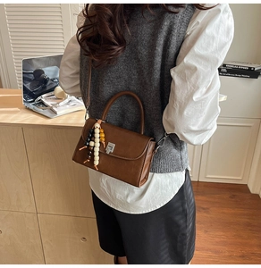 Close-up of retro brown PU leather handbag with silver clasp and beaded pendant detail