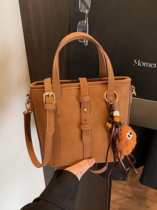 Braune Wildleder-Eimertasche mit Henkel und Plüsch-Anhänger vor einem Innenhintergrund