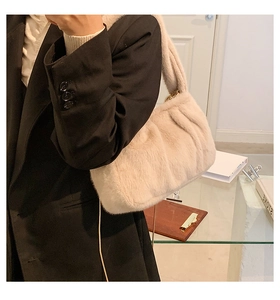 Détail du sac à bandoulière en peluche crème avec plis nuages porté sur un blazer noir