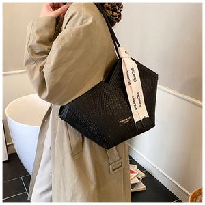 Détail d'un cabas noir à texture tressée avec ruban décoratif et plaque en métal dorée