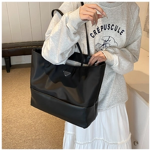 Close-up of black nylon tote bag featuring a triangular metal logo and reinforced base