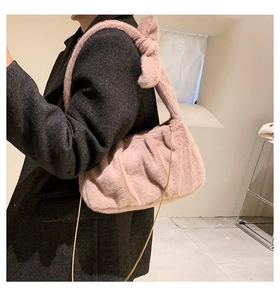 Détail du sac à bandoulière en peluche rose avec nœud et chaîne dorée sur un manteau