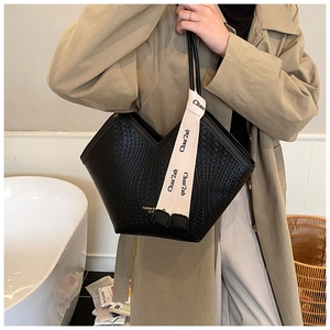 Détail du sac cabas tressé noir avec ouverture en V et ruban décoratif à logo