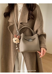 Close-up of taupe lychee leather handbag texture with plush bear charm and silver buckle