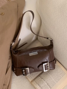Retro dark brown shoulder bag with silver buckles on a cozy sofa setting