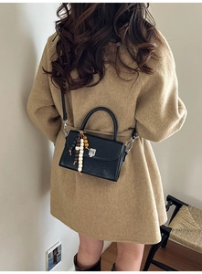 Detail of black leather handbag with wooden bead charm on a khaki wool coat