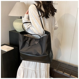 Detail of a large black nylon tote bag with shoulder straps worn in a home setting