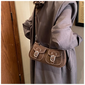 Detail of brown suede shoulder bag featuring dual front pockets and silver buckles