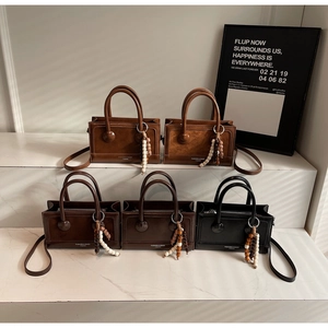 Detailed display of square leather handbags in brown and black with bead charms