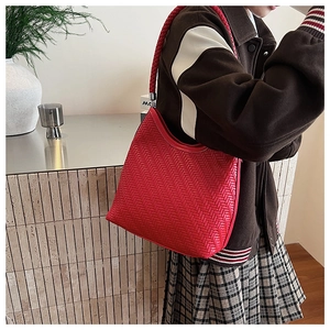 Detail of red woven bucket bag with thick shoulder strap shown on a model