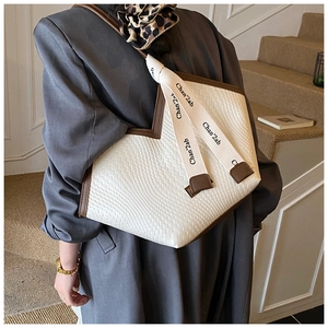 Détail d'un grand sac cabas tissé crème avec bandoulière à nœud et bords en cuir marron