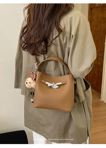 Brown litchi grain bucket bag with teddy bear pendant shown on model in trench coat